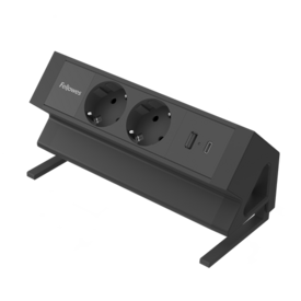 Lange, rechteckige schwarze Elektrifizierungseinheit mit zwei 230V-Anschlüssen und zwei USB-Anschlüssen. Die Einheit steht in einem 45°-Winkel und wird mit einer Klemme am Schreibtisch befestigt.
