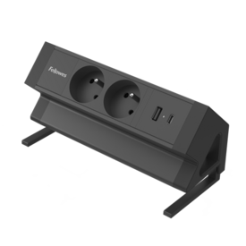 Unité d'alimentation rectangulaire noire longue avec deux ports 230V et deux connexions USB. L'unité est inclinée à 45° et équipée d'une pince en dessous pour la fixer à un bureau.  
