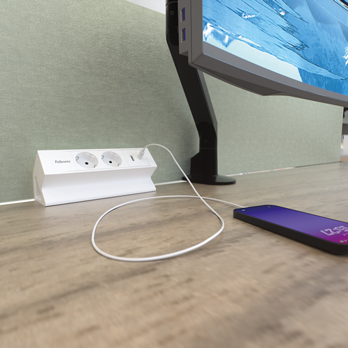 Lange rechteckige weiße Elektrifizierungseinheit mit zwei 230V-Anschlüssen und einem Keystone-Slot. Die Einheit steht im 45°-Winkel und wird mit einer Klemme an einem Tisch befestigt.