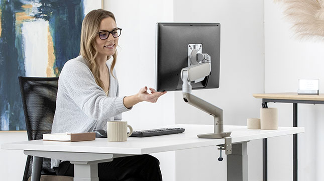 Woman sitting at her desk adjusting her screen position